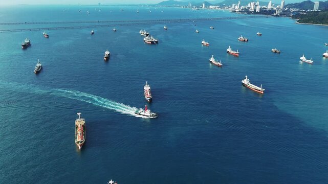 Fleet of oil tanker ships and commercial cargo vessels anchored in the deep blue sea near a long bridge. Global maritime logistics, international shipping trade, and energy transport.