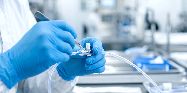Skilled medical device manufacturing technician wearing sterile cleanroom attire, carefully connecting catheter tubing to a sterile medical component with precision inside a production facility.