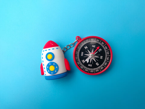 A toy rocket keychain is attached to a red magnetic navigation compass over a blue background