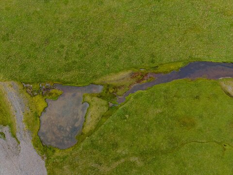 Aerial view of a winding stream and small pond set within lush green meadows in the volcanic landscape of Snaefellsnes, Snaefellsbaer, Iceland.