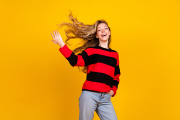 Charming young woman in a striped sweater posing cheerfully against a vibrant yellow background,...