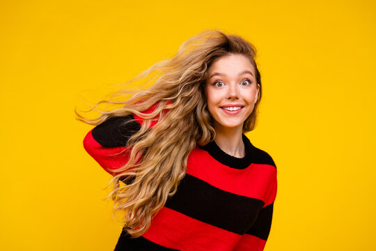 Charming young woman in a striped sweater posing against a yellow background radiating happiness and cheerfulness