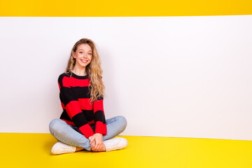 Adorable young woman sitting cheerfully in casual clothes against a vibrant yellow background,...