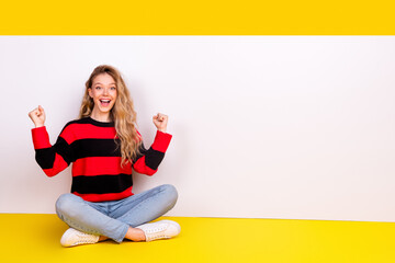 Cheerful young woman in a striped sweater posing joyfully against a vibrant yellow backdrop,...