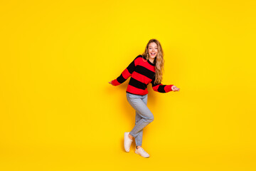Charming young woman wearing a striped sweater posing cheerfully against a vibrant yellow...