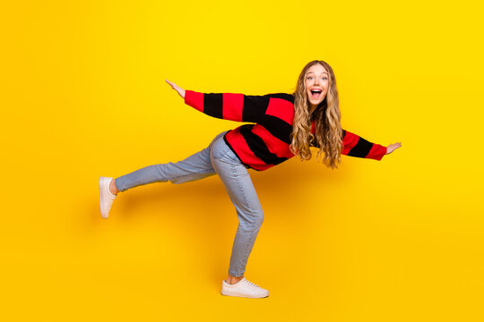 Cheerful young woman in a vibrant striped sweater posing on a yellow background, radiating happiness and modern casual style