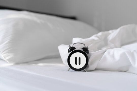 black alarm clock with pause sign on messy bed with morning light, for take a break, relaxation, overworked concept, hormone replacement therapy