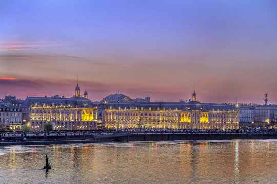 Illuminated Place de la Bourse facade viewed from across Garonne river at sunset in Bordeaux, France. Grand night illumination