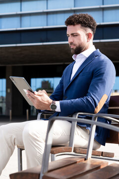 Businessman using digital tablet while sitting outside modern office building