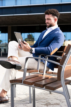 Businessman using digital tablet while sitting outside modern office building