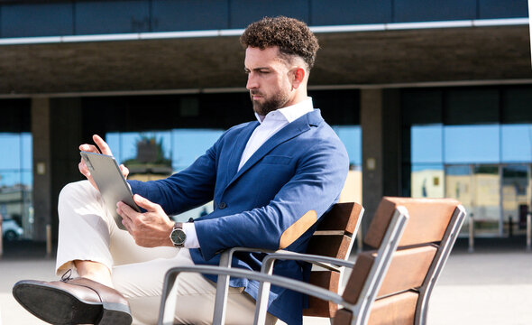Businessman using digital tablet while sitting outside modern office building