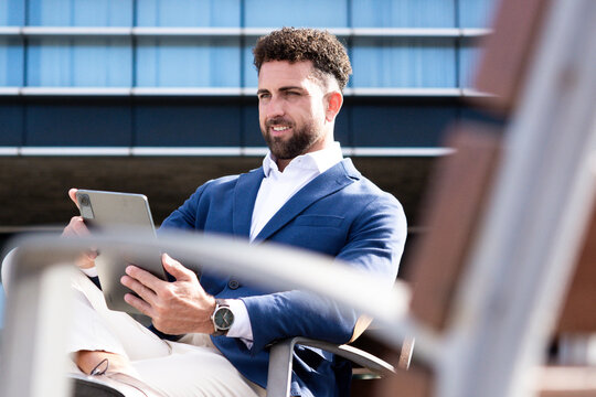 Businessman using digital tablet while sitting outside modern office building