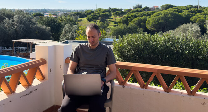 Man using laptop on lounge chair at poolside