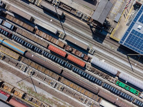 Aerial view of Chiasso Cargo Train Terminal featuring various freight train cars on multiple tracks and a building with solar panels in Chiasso, Ticino, Switzerland.