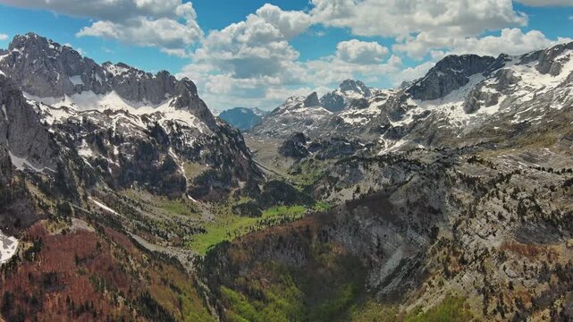 Aerial view of amazing rocky mountains in snow and green valley, Prokletie park, Montenegro and Albania, 4k