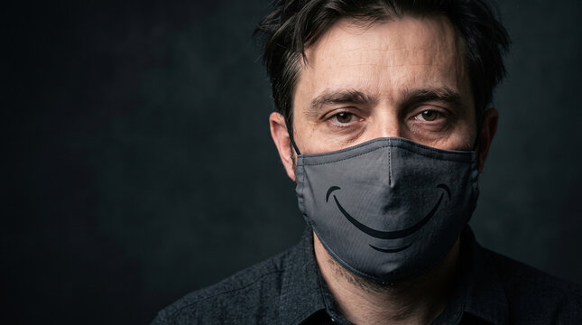A tired male employee, but wearing a mask of a smile to hide the truth. The concept of workplace burnout and self-deception through a mask, with space for copying.