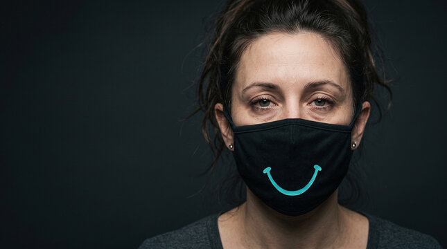 A tired female employee, but wearing a mask of smiles to hide the truth. The concept of workplace burnout and self-deception through masks, with space for copying.