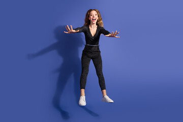 Happy young woman jumps and smiles in a shiny striped jumpsuit against a blue background