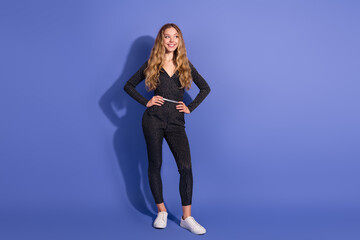 Young stylish woman in striped jumpsuit with white sneakers posing against blue background