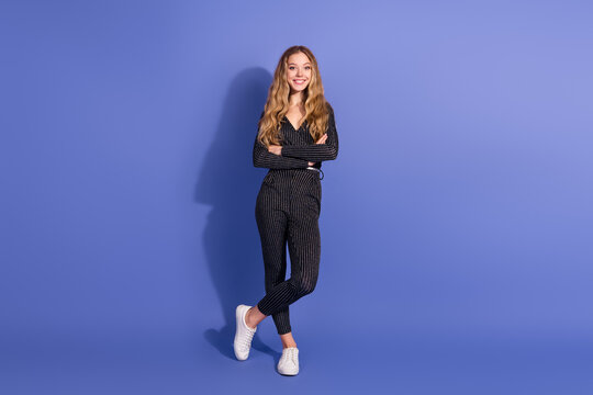 Young fashion model wearing a striped jumpsuit stands confidently against a violet blue background with a bright smile and casual stylish vibe
