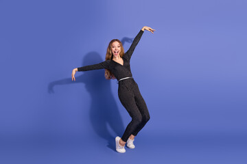 Naklejka premium Young stylish woman in striped jumpsuit dances and smiles against a violet background for lifestyle fashion advertising and retail styling