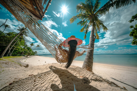Woman tourist stay under shadow of the coconut trees at the edge of the sea beach, cheerfully traveling life in summer of the island
