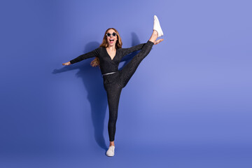 A fun stylish woman kicks high in a striped jumpsuit against a blue background showcasing fashion...