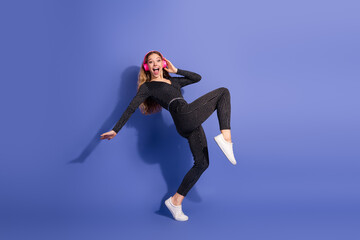 Naklejka premium Young stylish woman in striped jumpsuit wearing pink headphones jumps and smiles against a solid blue background for a vibrant fashion lifestyle image