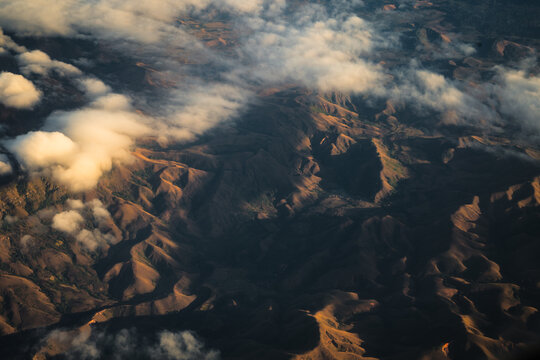 Aerial view of the rugged mountainous landscape featuring rolling hills, deep valleys, and scattered clouds illuminated by the soft light of the golden hour Madagascar.