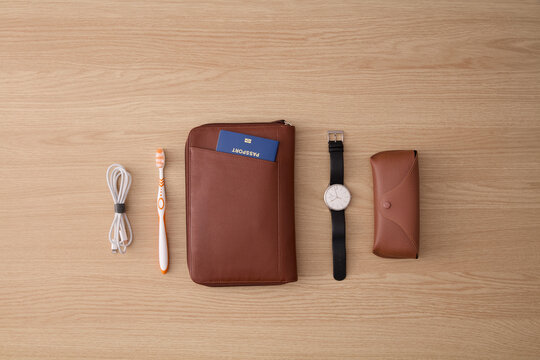 Flat Lay of Travel Essentials with Passport, Leather Pouch, Watch, and Accessories on Wooden Table