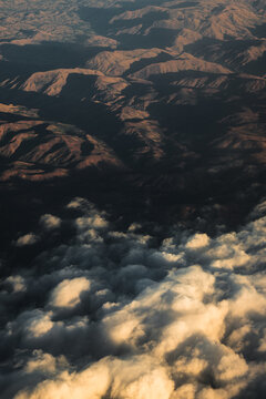 Aerial view of the rugged mountainous landscape during golden hour, with soft clouds partially obscuring the peaks in Madagascar.