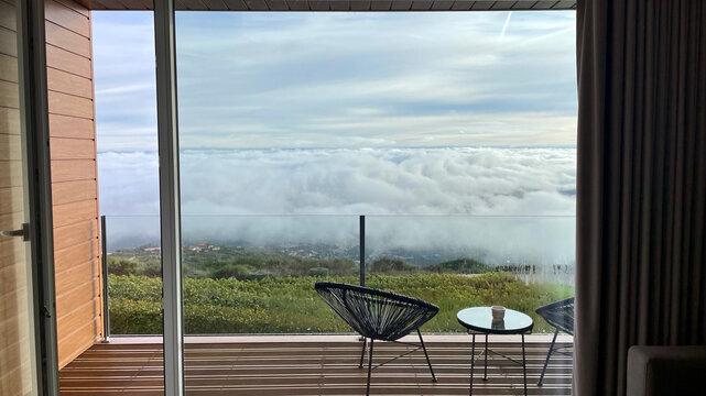 Breathtaking view of a sea of clouds and mountains from a modern balcony terrace with patio chairs and coffee table