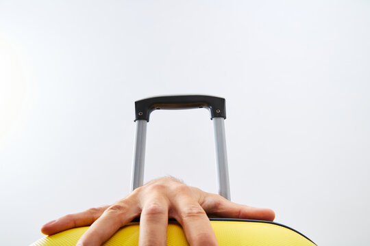 Male hand resting on yellow suitcase luggage handle ready for travel