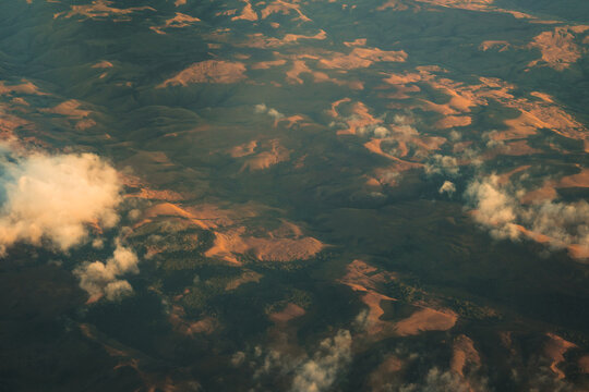 Aerial view of the rugged, rolling mountainous landscape during the golden hour, with soft clouds casting shadows over the terrain in Madagascar.