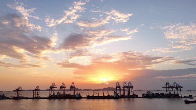 Silhouettes of gantry cranes and cargo ships at a bustling seaport during a dramatic golden sunset. Global maritime logistics, international trade, and industrial shipping transport concept.