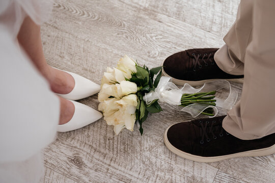 Wedding bouquet of white roses lying on a wooden floor between the feet of the bride and groom