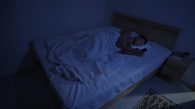 Man endlessly scrolling short form videos on smartphone in bed at night, compulsive social media use and screen addiction
