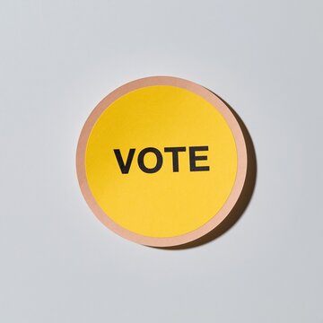 Round vote sticker with a yellow center and terracotta rim, featuring a tactile matte finish on a clean white background for civic engagement and election mockups