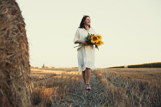 woman in a white dress holding a bouquet of wild flowers with sunflowers in a field
