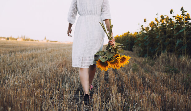 woman in a white dress holding a bouquet of wild flowers with sunflowers in a field
