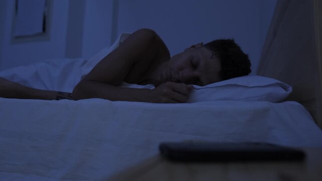 Man repeatedly checking smartphone after trying to sleep, compulsive phone use, digital addiction and bedtime procrastination at night