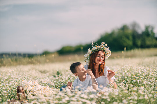 Summer meadow relaxation with mother and young son sitting among blooming white daisies in sunny countryside
