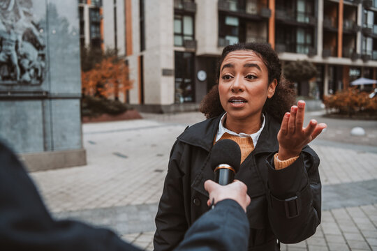 African American woman outdoors in the city center speaks to a reporter during autumn, wearing a coat and expressing emotions