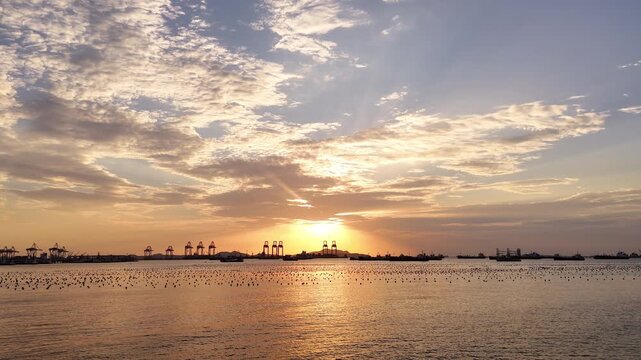 Silhouettes of gantry cranes and cargo ships at a bustling seaport during a dramatic golden sunset. Global maritime logistics, international trade, and industrial shipping transport concept.