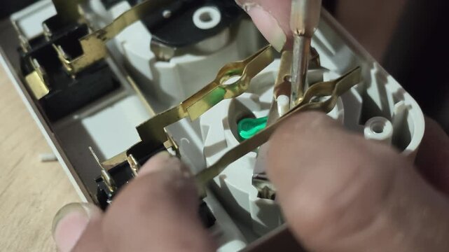Detailed view of an electrician using a small tool to align internal brass metal contact strips inside an opened power strip casing during repair work.
