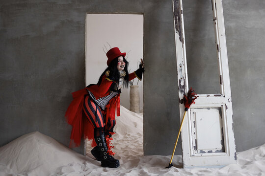 Costumed ringmaster standing beside old mirror and door frame in sand filled grey ruin