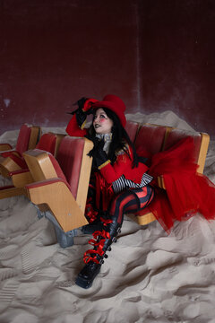 Woman in red top hat looking upward while seated among ruined red cinema chairs