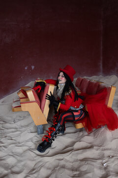 Pensive circus character sitting between broken theatre chairs with hands clasped together