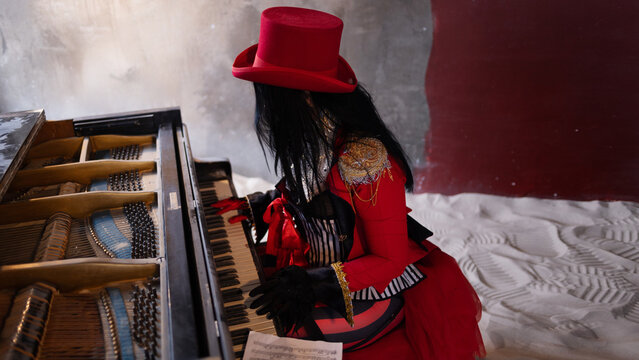 Costumed pianist in red playing an old upright piano half buried in drifting sand