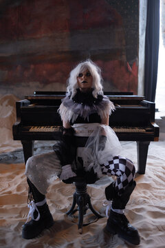 Pale harlequin figure seated at grand piano in sand covered abandoned hall